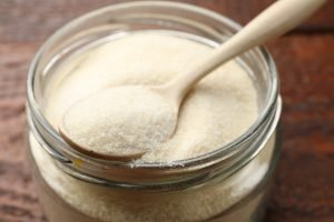 Gelatin powder and spoon in jar on wooden table, closeup